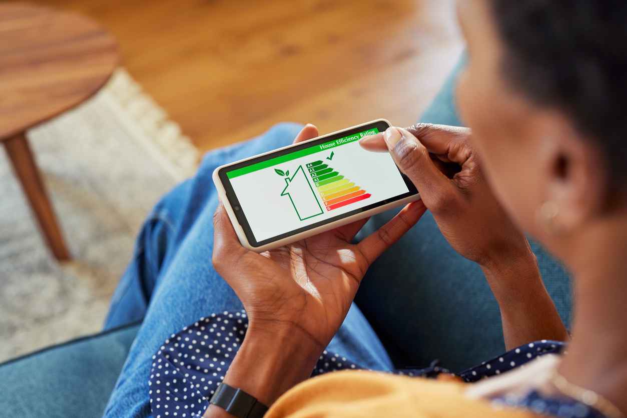 Close up of woman holding smartphone with energy efficiency chart and class on screen. Female hands holding smart phone and looking at house efficiency rating. Concept of ecological, eco renovation and bio energetic house.