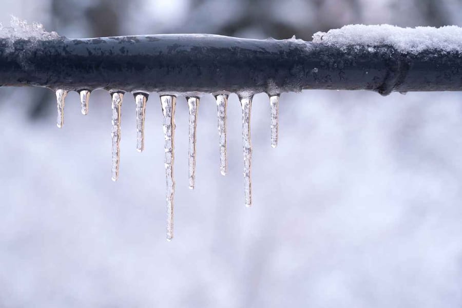 Frozen icicles on a gray pipe after a thaw in winter